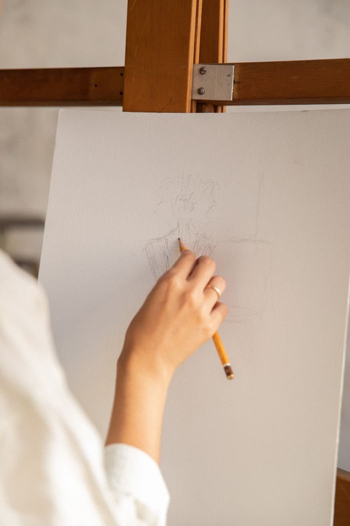 Close-up of an artist's hand sketching with a pencil on a canvas, showcasing creativity.